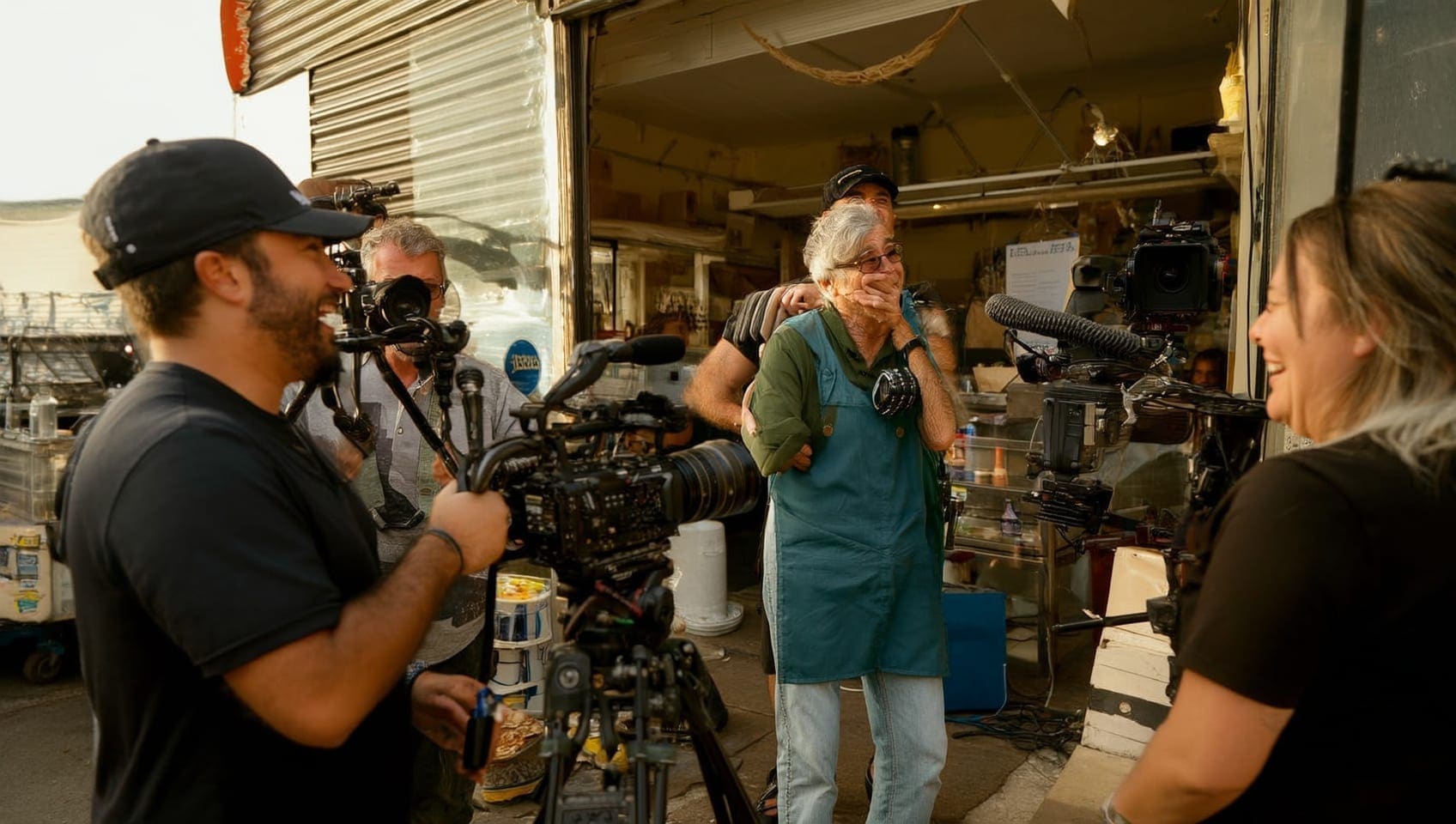 A JULY production crew filming on location, camera and microphone in motion around a laughing colleague