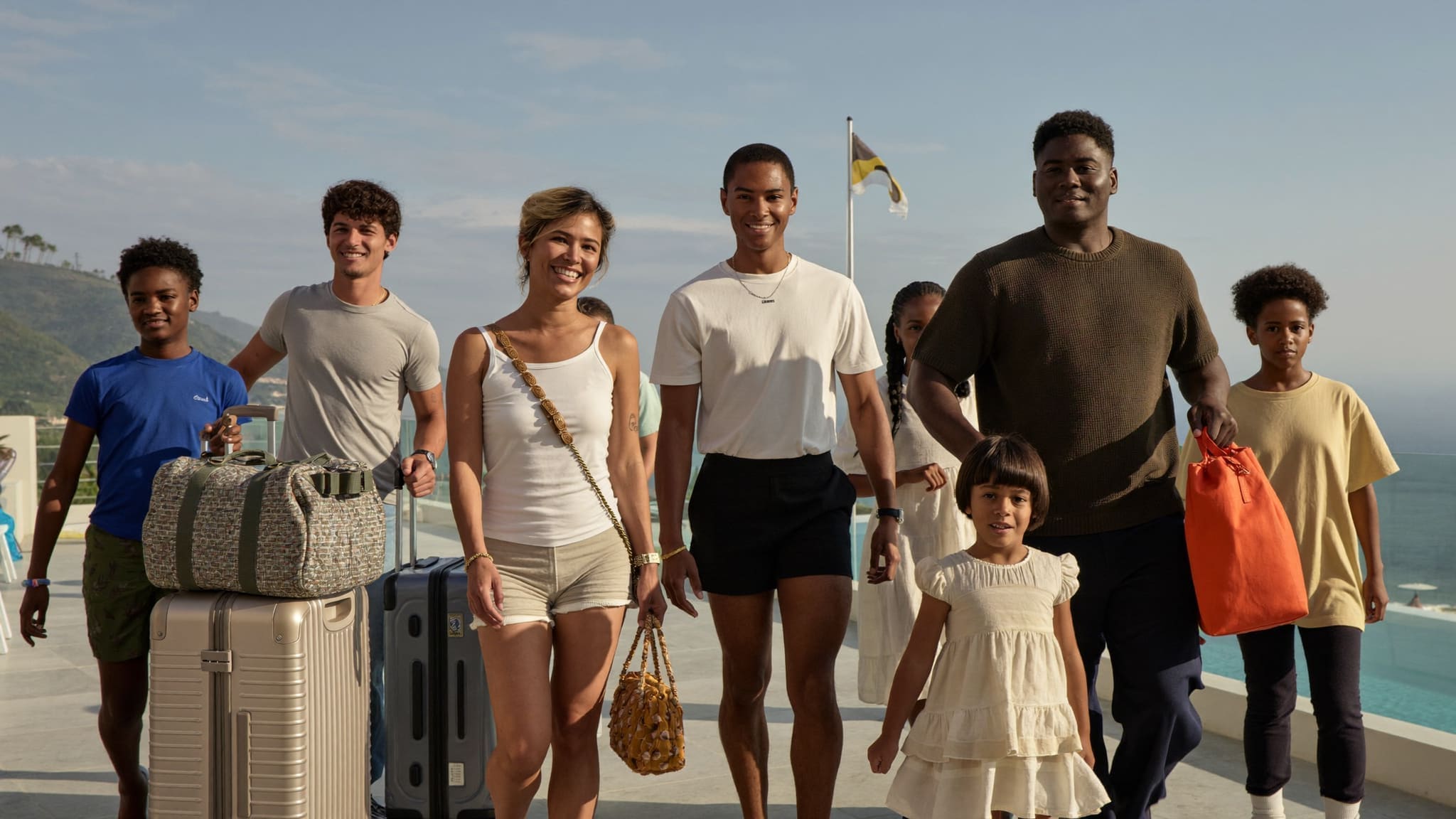 Travelers of different ages arriving on a resort terrace at golden hour, luggage beside them and the view opening ahead
